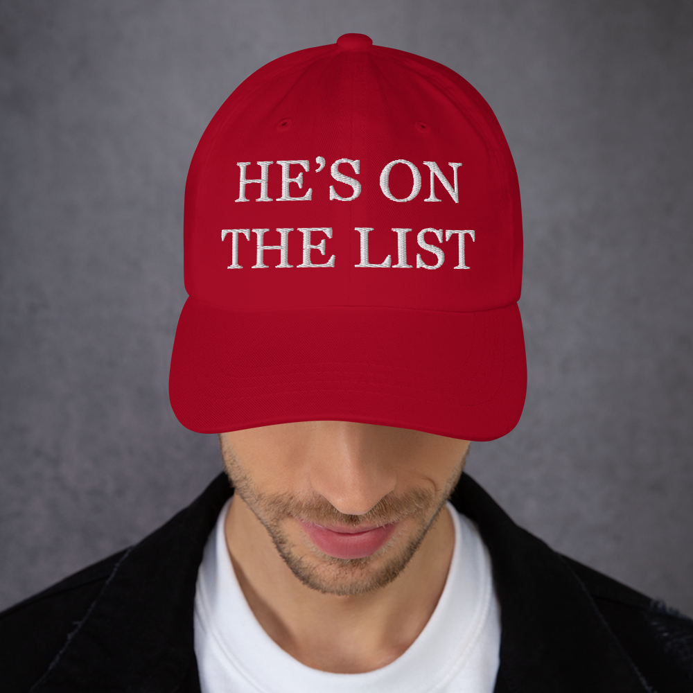 Red cap with 'HE'S ON THE LIST' text worn by a person against a gray background